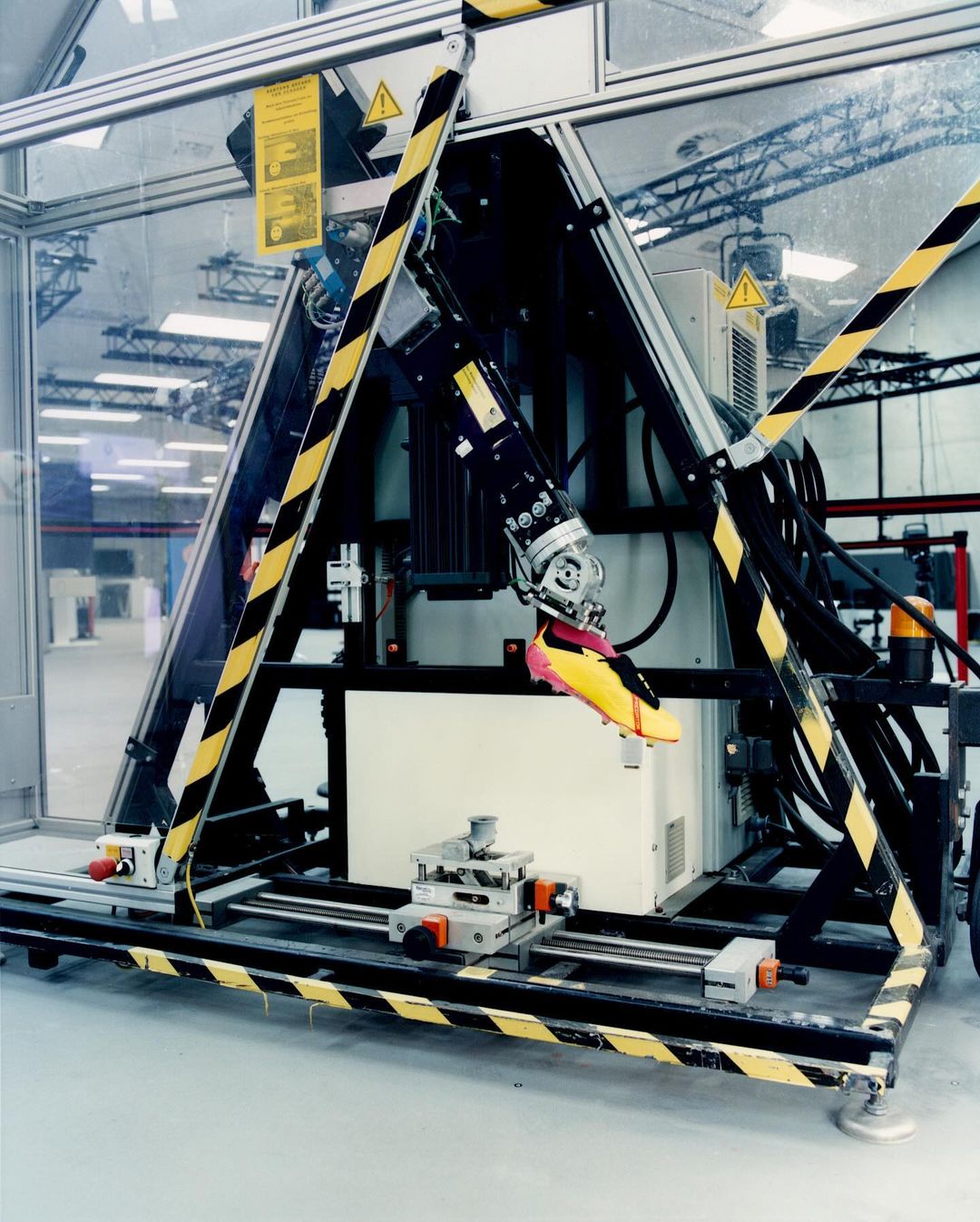 Automated manufacturing machine holds a soccer shoe for testing in a factory setting, showcasing advanced industrial technology and precision.