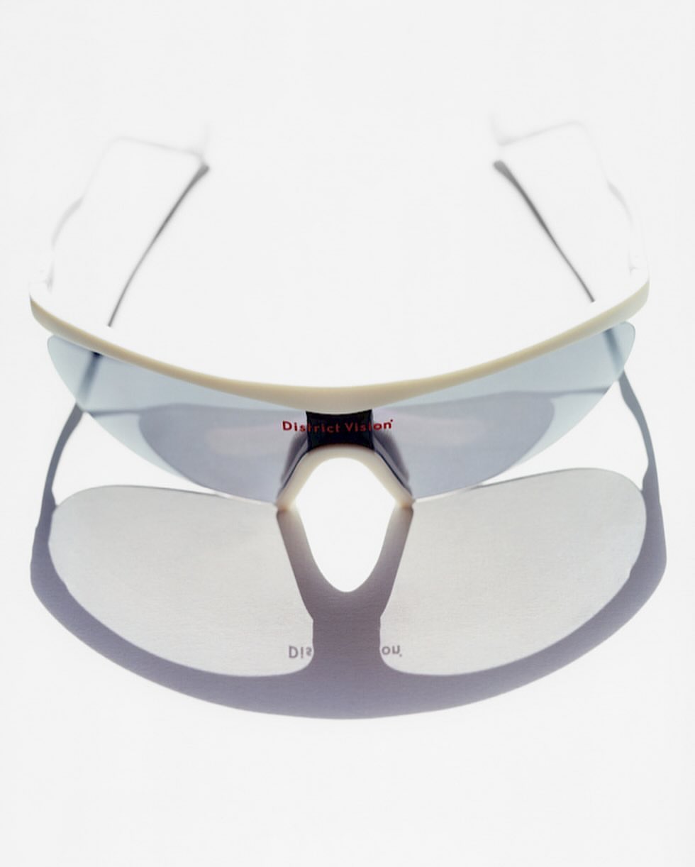 Close-up studio shot of rimless white District Vision sunglasses featuring blue mirrored lenses and the company's logo in red.