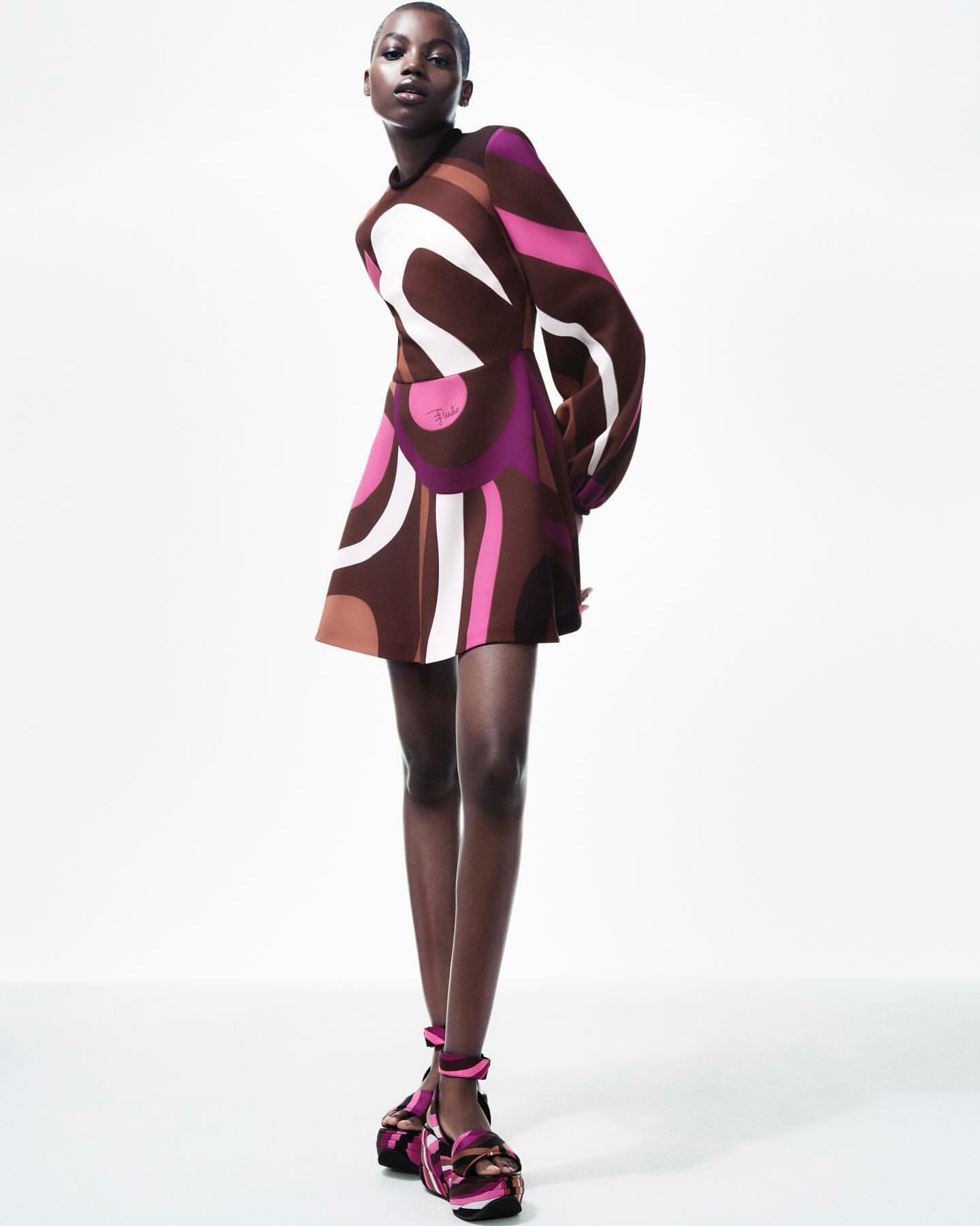 Elegant Black model wears a retro-patterned brown, pink, and white mini dress with chunky platform Mary Janes against a white backdrop.