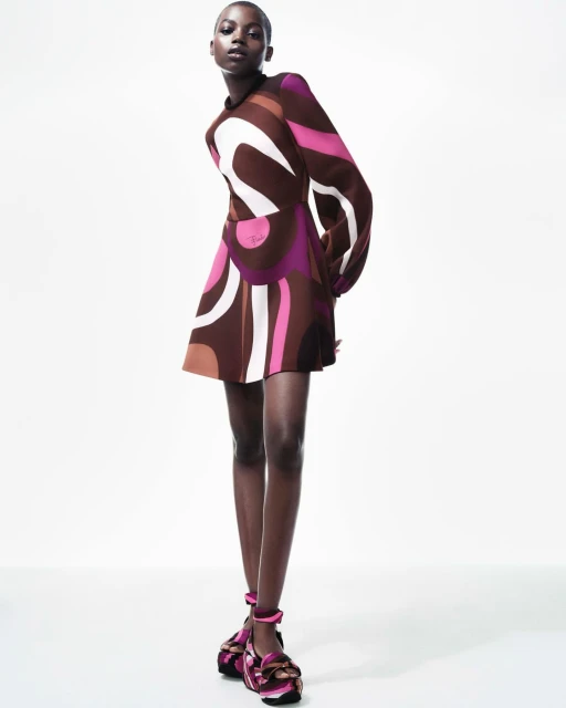 Elegant Black model wears a retro-patterned brown, pink, and white mini dress with chunky platform Mary Janes against a white backdrop.