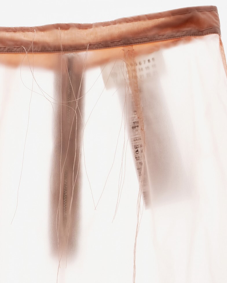 Close-up of a translucent fabric skirt with a brown waistband and loose threads, softly lit against a bright background.