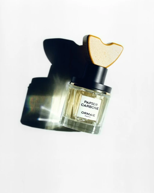 Perfume bottle of Papier Carbone by Ormaie Paris, a fragrance with a wooden stopper, against a white background, casting a dark shadow.