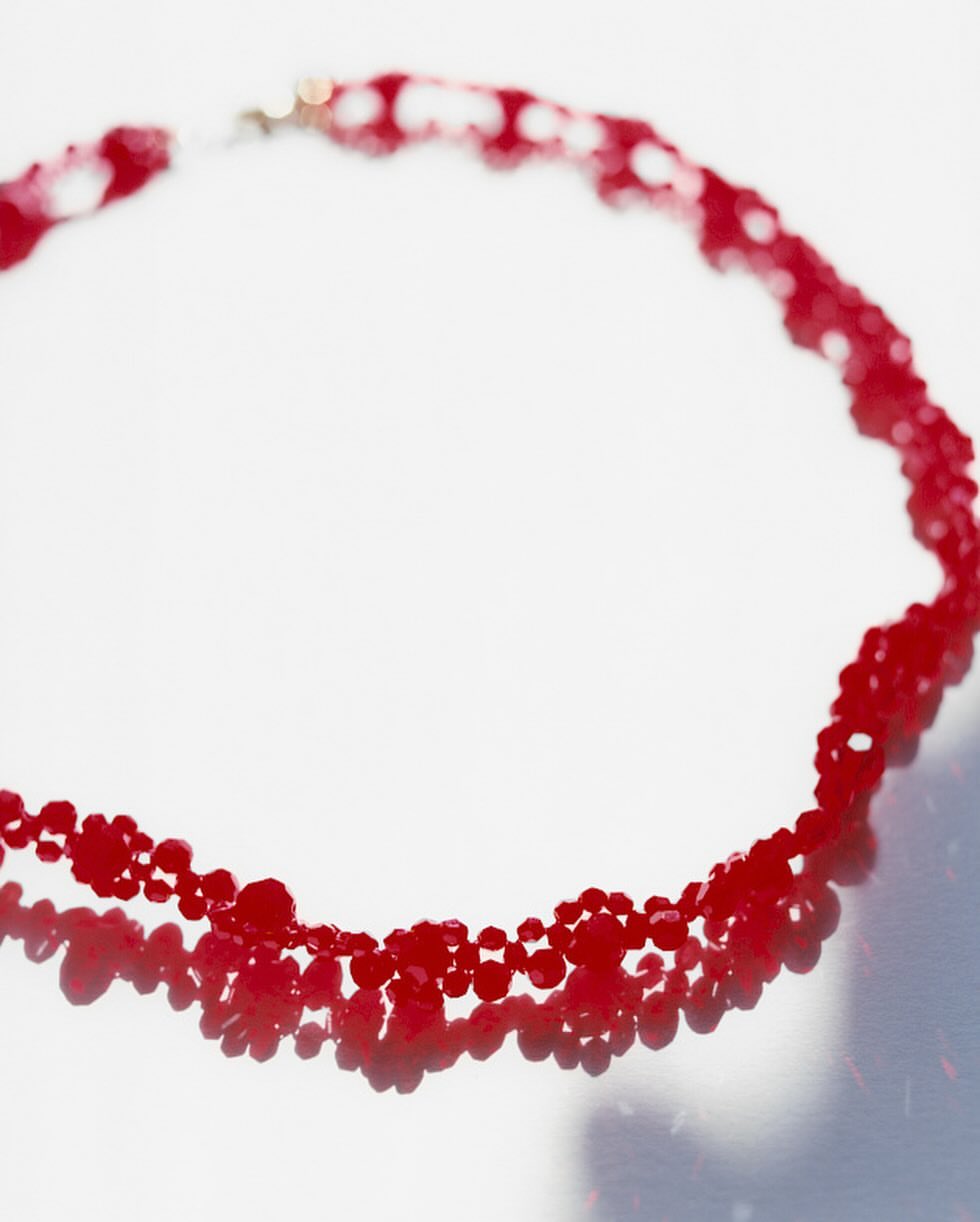 Close-up of a beaded necklace made of red beads, casting a shadow on a bright white surface, showcasing jewelry and design.