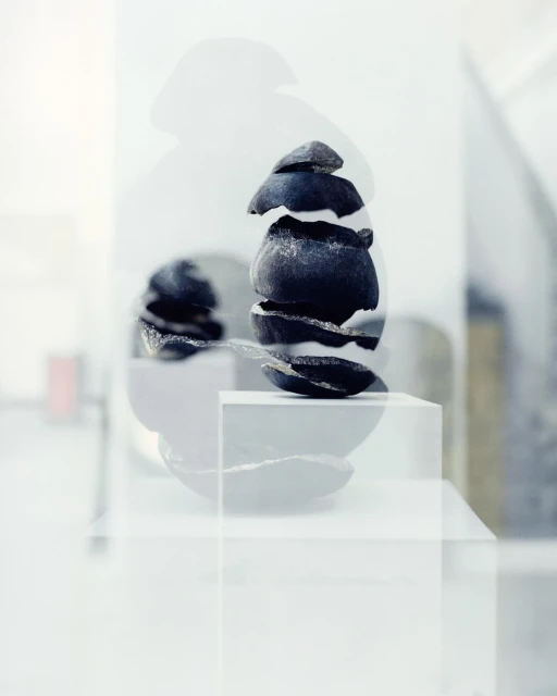 Abstract still life of stacked dark stones on white pedestals with a muted indoor background, creating a serene and minimalist aesthetic.