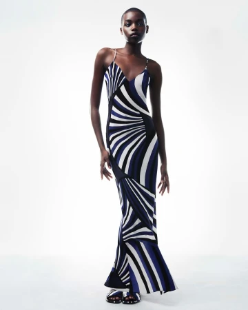 Elegant adult woman in a modern, striped maxi dress poses in a bright photo studio. Fashion editorial image with a minimalist background.