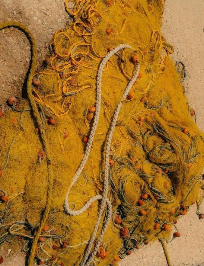 A vibrant yellow fishing net with orange buoys and a white rope, spread across a textured surface in bright, natural lighting.