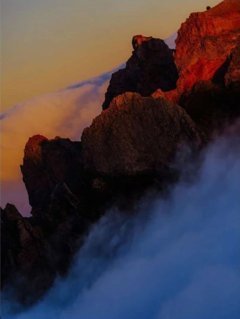 Dramatic mountain landscape with cloud cover. Jagged cliffs in warm light contrast with cool blue clouds at sunset.