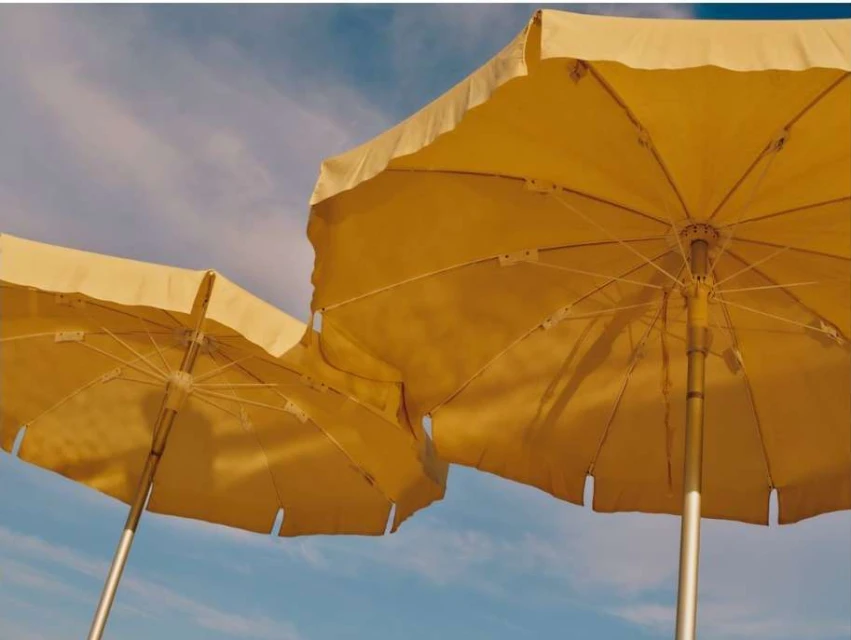 Two yellow beach umbrellas under a blue sky with wispy clouds, viewed from below, evoke a sunny day at the seashore.