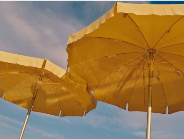 Two yellow beach umbrellas under a blue sky with wispy clouds, viewed from below, evoke a sunny day at the seashore.