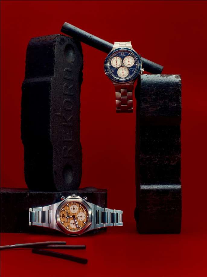 Two stainless steel watches on black stands and rods against a red backdrop create an industrial, stylized horology display.