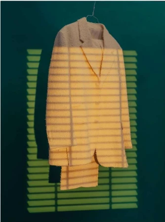 Suit hanging on a hanger against a green wall with sunlight and shadows casting horizontal lines creating a unique visual effect.