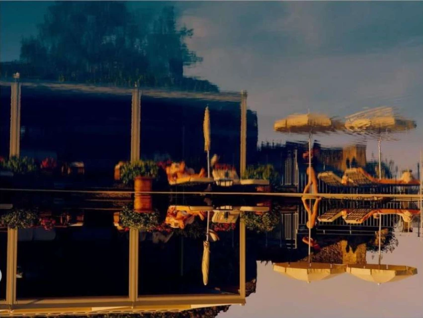 Upside-down shot features a building reflection on water, showcasing architectural details and nearby trees in a unique visual perspective.