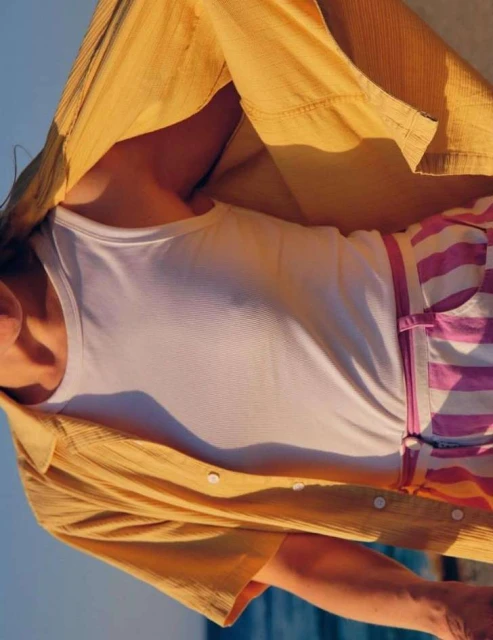 A person wearing a white tank top, pink striped shorts, and a yellow button-down shirt is partially visible. Sky in the background.