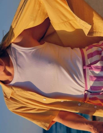 A person wearing a white tank top, pink striped shorts, and a yellow button-down shirt is partially visible. Sky in the background.