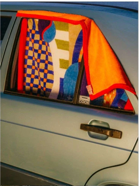Close-up of a blue car with an open back window, colorful towels hanging in the window, and a silver car door handle.
