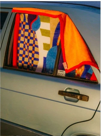 Close-up of a blue car with an open back window, colorful towels hanging in the window, and a silver car door handle.