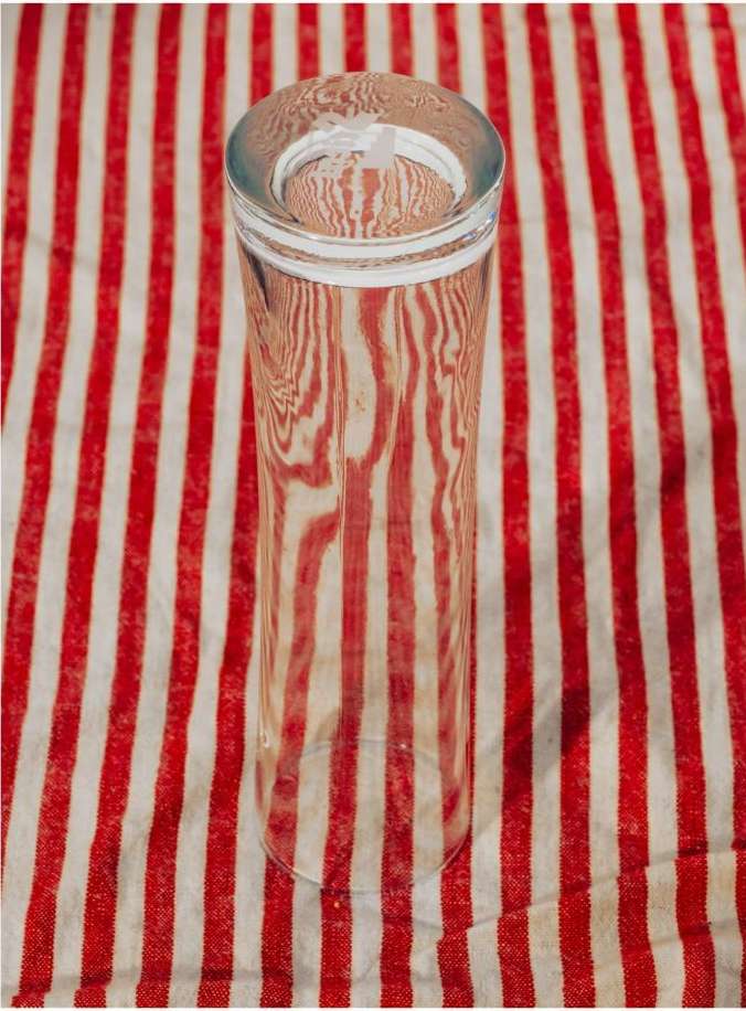 Clear glass vase sits centered against a striped red and white background, reflecting pattern and light with subtle distortion.
