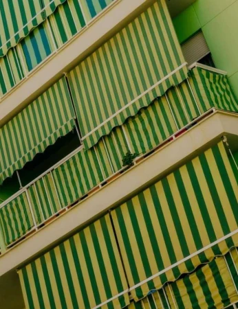 Exterior view of a building with multiple balconies covered in striped green and white awnings, creating a rhythmic pattern of light and shadow.