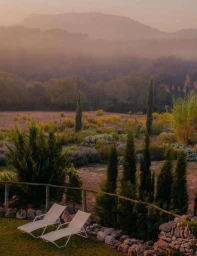 Two white lounge chairs overlooking a hazy landscape with trees and rolling hills in the background at sunrise.