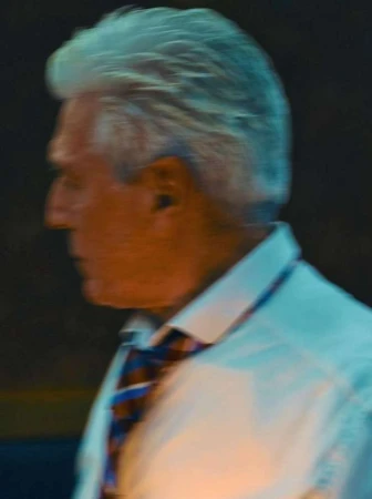 Profile shot of an elderly man with silver hair wearing a white shirt and patterned tie under cool lighting