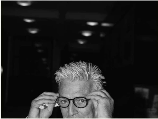 Close-up black and white portrait of a man adjusting his round eyeglasses, captured by photographer Maximilian Virgili.