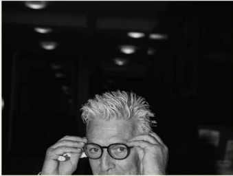 Close-up black and white portrait of a man adjusting his round eyeglasses, captured by photographer Maximilian Virgili.