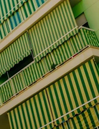 Low-angle architectural shot of a residential building exterior featuring green and yellow striped striped awnings and balconies