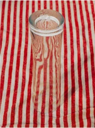 An inverted clear glass standing upright on a red and white vertically striped fabric surface