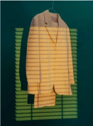 Textured cream jacket hanging against a dark green wall with horizontal window blind shadows cast across it.