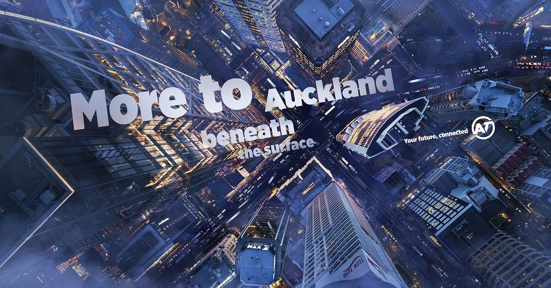 Aerial view of Auckland city buildings at dusk. Modern architecture lit up against a blue sky. White text overlay.