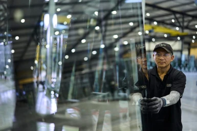 Man wearing a black shirt and cap holding a large sheet of glass inside a warehouse in Auckland