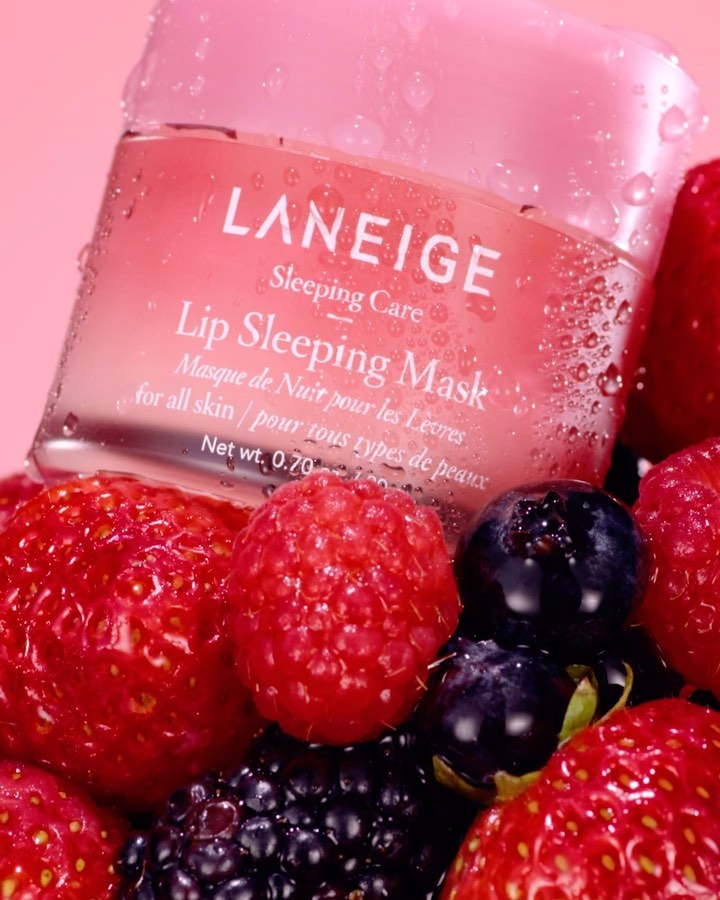 Close-up of Laneige lip sleeping mask on bed of strawberries, raspberries, blackberries, blueberries, and water droplets. Beauty product.