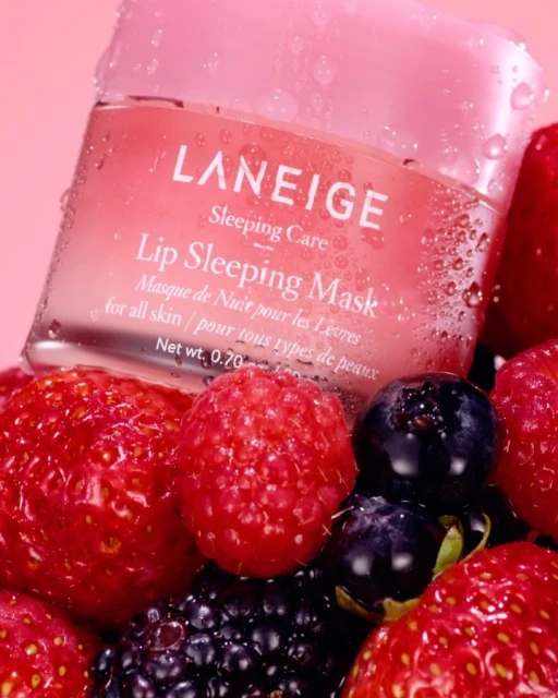 Close-up of Laneige lip sleeping mask on bed of strawberries, raspberries, blackberries, blueberries, and water droplets. Beauty product.