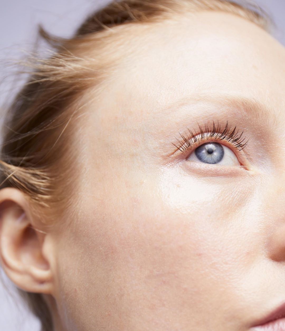 Close-up studio shot of fair-skinned adult woman with light blue eye, looking right. Soft skin texture, with blonde hair and eyelashes.