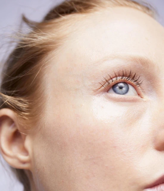 Close-up studio shot of fair-skinned adult woman with light blue eye, looking right. Soft skin texture, with blonde hair and eyelashes.