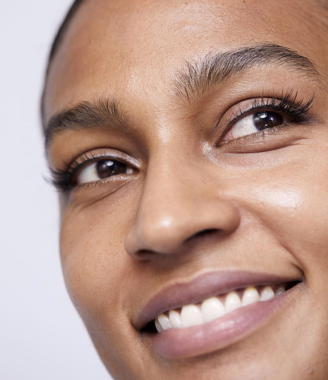 Close-up shot of a smiling adult female with tan skin, showcasing clear skin, healthy teeth, and defined eyebrow features.