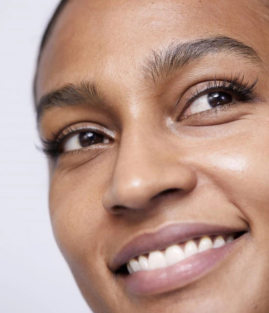 Close-up shot of a smiling adult female with tan skin, showcasing clear skin, healthy teeth, and defined eyebrow features.