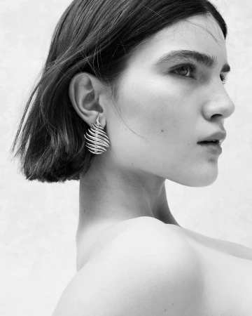 Profile portrait of a brunette woman wearing a large sculptural silver earring against a neutral background
