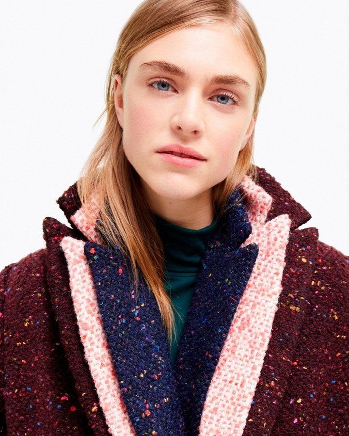 Blonde woman in a colorful, oversized coat with a green turtleneck, photographed in a studio setting with bright, even lighting.