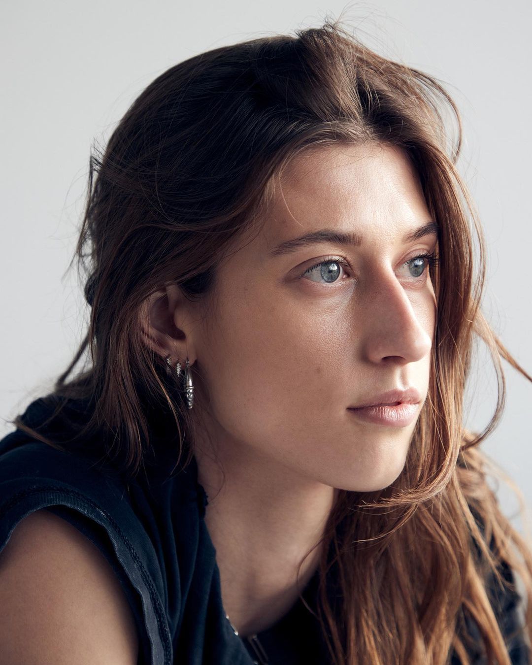 Portrait of a woman with long brown hair wearing hoop earrings against a neutral background by photographer Mei Tao