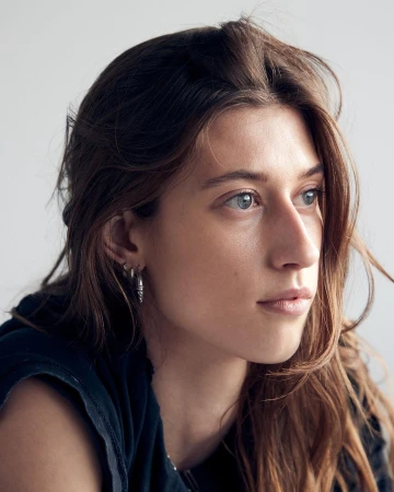 Portrait of a woman with long brown hair wearing hoop earrings against a neutral background by photographer Mei Tao