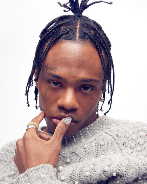 Close-up studio shot of a Black male model with braided hair wearing a pearl-embellished sweater, gazing at the camera with a neutral expression.