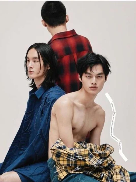 Three fashionable young adult males pose in a studio wearing stylish shirts and jeans in a vertical portrait with white background.