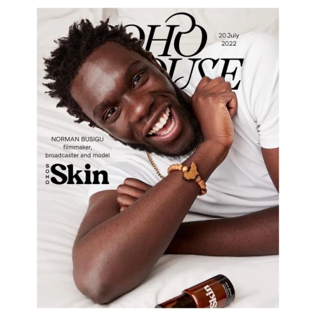 Magazine cover featuring a smiling Black man with a wooden bracelet, laid on a bed with a drink bottle in the foreground.