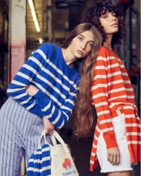 Two women posing together indoors wearing striped sweaters, one in blue stripes and one in orange stripes, photographed by Mei Tao.