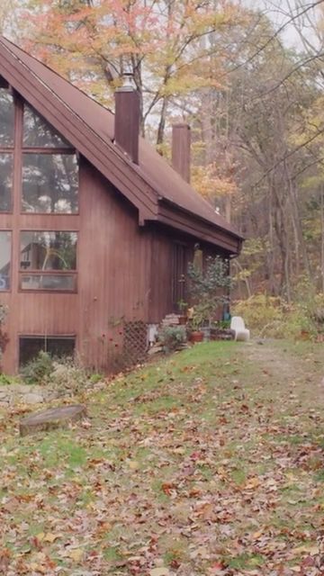 Exterior view of an A-frame house featuring a steeply angled roof, a wall of windows, and a lush, green, autumn-colored yard with fallen leaves.