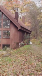 Brown wooden house with large windows nestled in an autumn forest covered in fallen leaves, photographed by Melanie Acevedo.