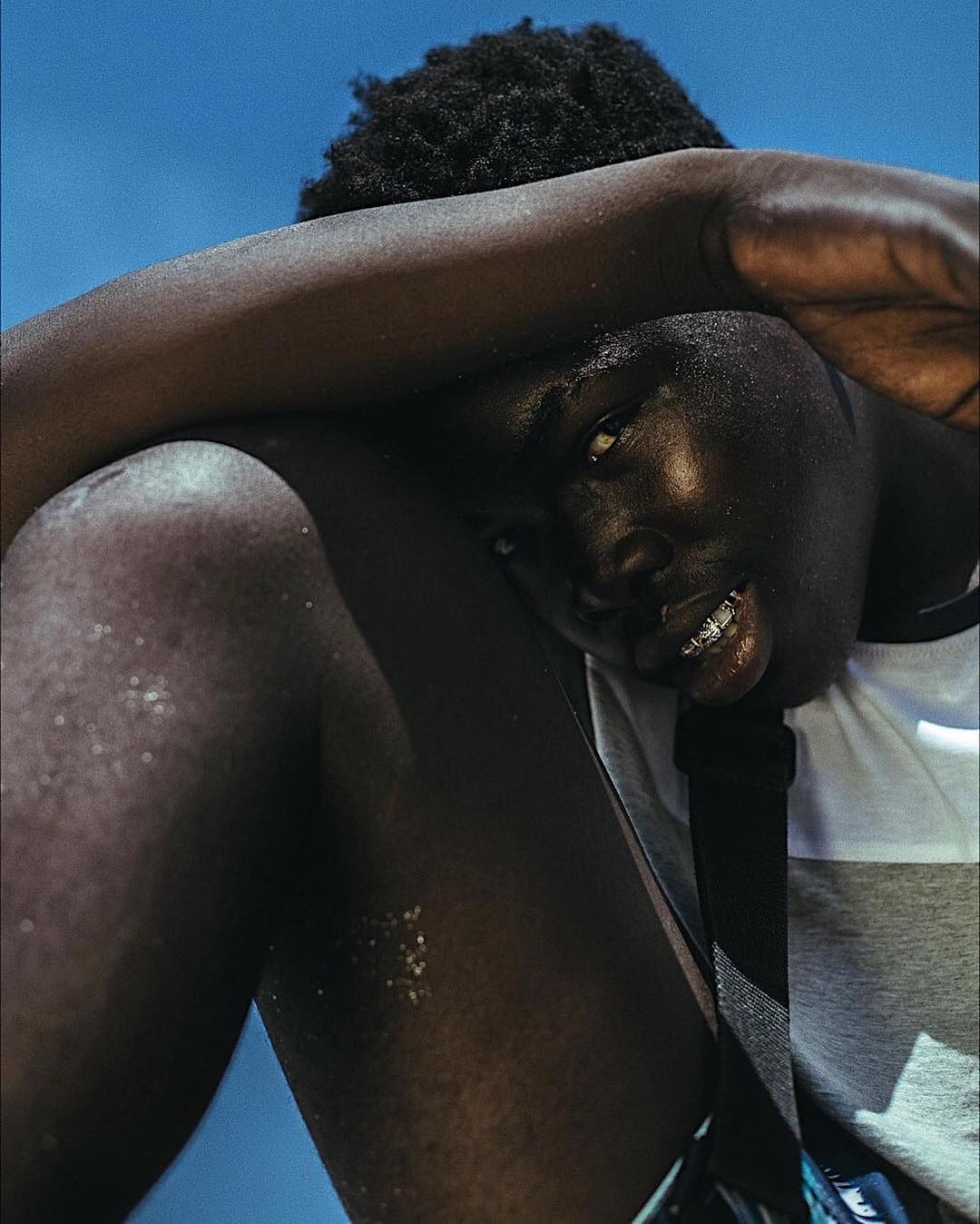 Young adult man with dark skin and braces posing outdoors against a clear blue sky, creating a striking and minimalist portrait.
