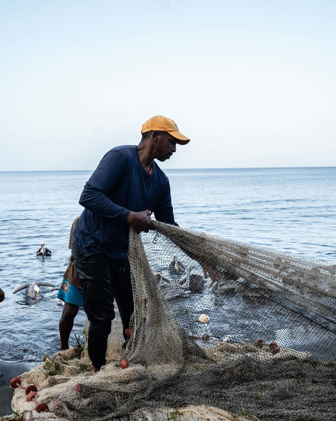 Fisherman retrieves fishing net filled with the day's catch on a beach with the ocean visible in the background on a cloudy day.