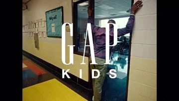 Adult male standing in a doorway with a Gap Kids logo and back-to-school poster in the background of a school hallway.